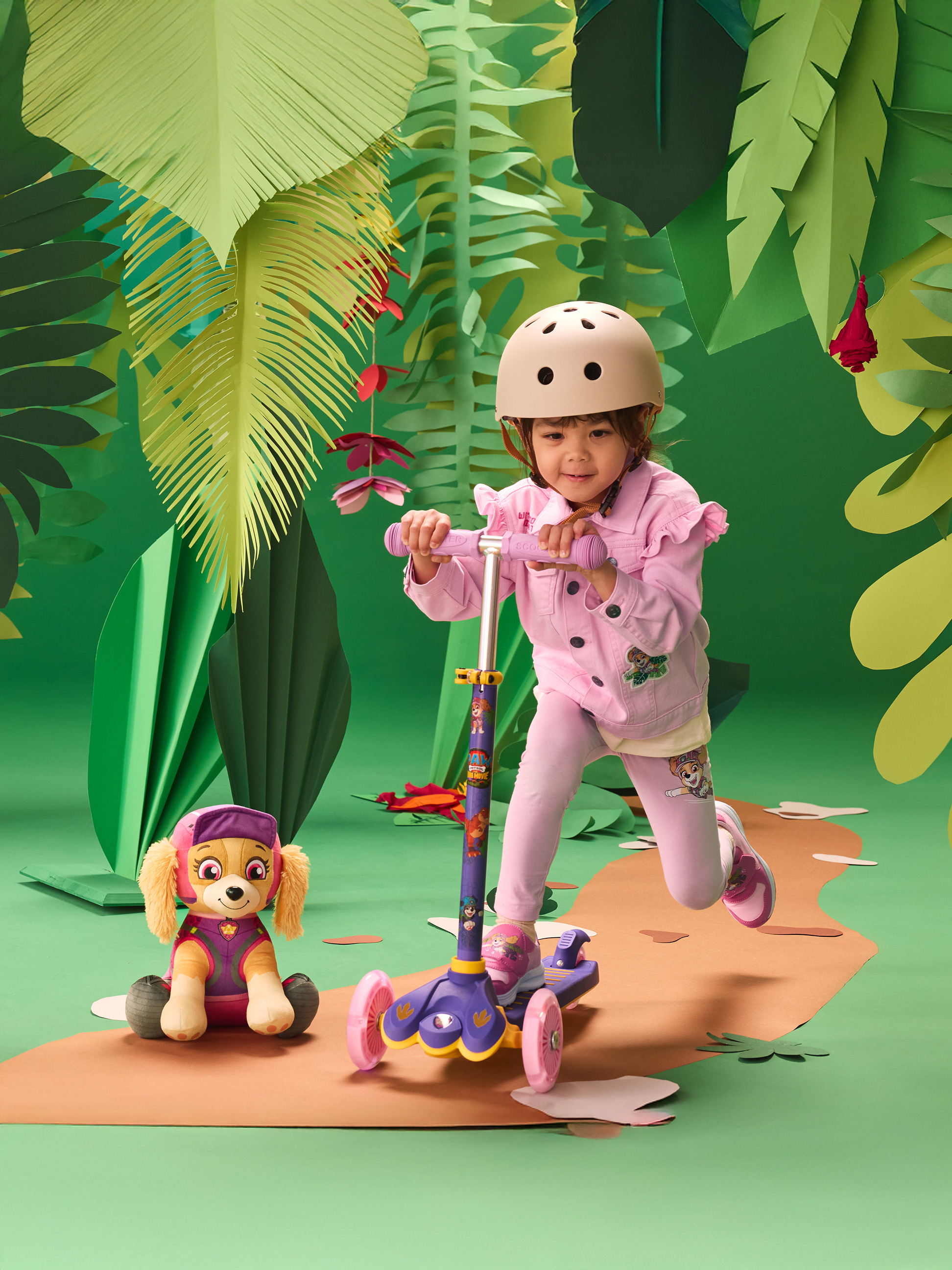 Meisje met helm op scooter, met knuffel, in jungle-omgeving.