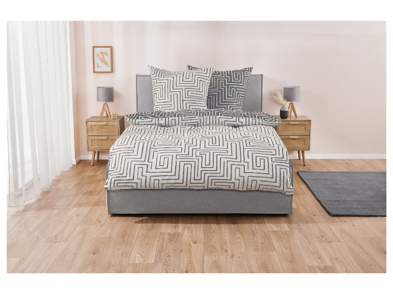 Grijs en beige beddengoed met labyrintpatroon op een grijs bed.