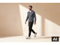 Lachende man loopt, draagt een grijze V-hals trui, zwarte broek en wit-blauwe sneakers.