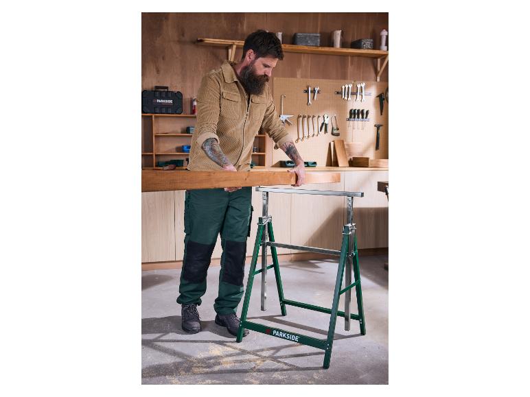 Man legt een houten plank op zaagbokken in een werkplaats.