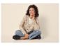 Vrouw in beige gebreid vest, jeans en zwarte loafers zit met gekruiste benen.