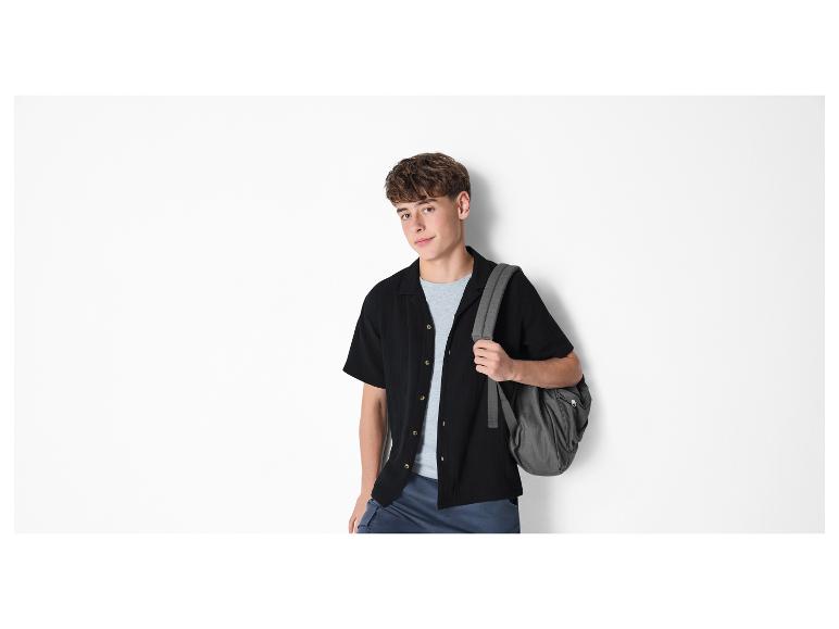 Jonge man in zwart overhemd, grijs T-shirt en rugzak.