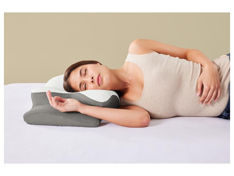 Vrouw slaapt op haar zij op een bed met een grijs en wit ergonomisch kussen.