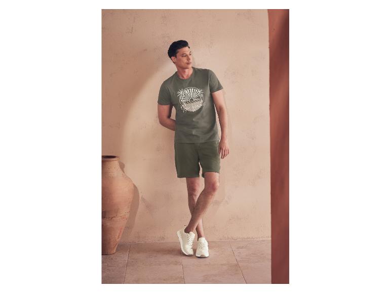 Een man in een groen t-shirt en korte broek, witte sneakers.