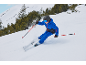Kind skiet in blauw skipak, met ski's, stokken, helm en bril op besneeuwde berg.