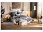 Slaapkamer met grijs beddengoed, beige bed, poef en houten vloer.