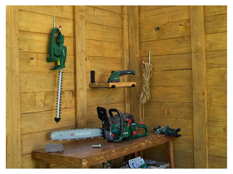 Tuinmachines in een houten schuur: kettingzaag, heggenschaar en schuurmachine.