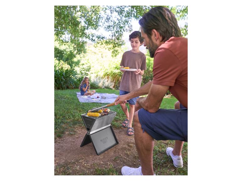 Vader en zoon barbecueën op een draagbare grill, meisje zit op een deken op de achtergrond.