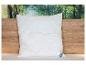 Een wit gewatteerd BeCo kussen op een bed met een houten hoofdbord en bosachtergrond.