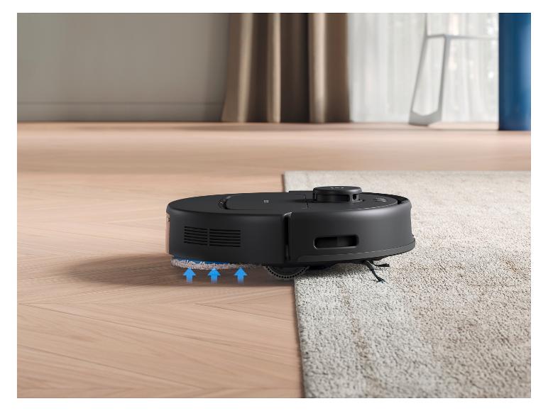 Een zwarte robotstofzuiger beweegt van een houten vloer naar een licht tapijt.