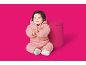 Blijde baby in een roze gewatteerd skipak, klappend in de handen naast een roze poef.