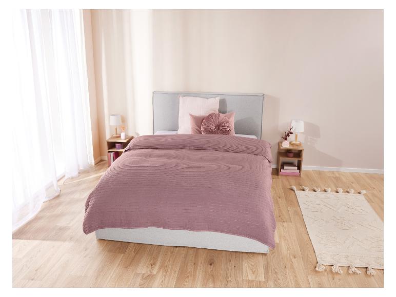 Bed met stoffig roze beddengoed en een boho chic kleed.