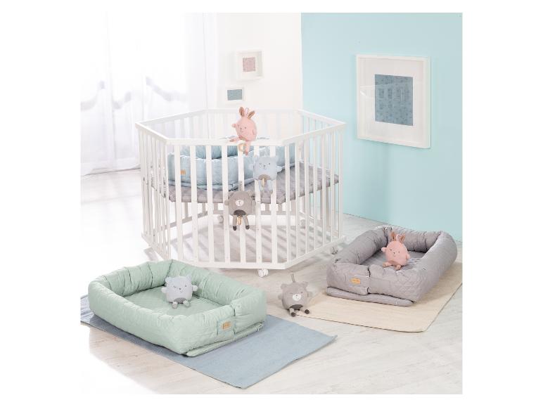 Wit zeshoekig babybedje met blauw matras, twee babynestjes met knuffels en vloerkleden.