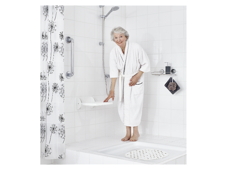Een oudere vrouw in een badjas gebruikt een opklapbare douchestoel in een moderne badkamer.