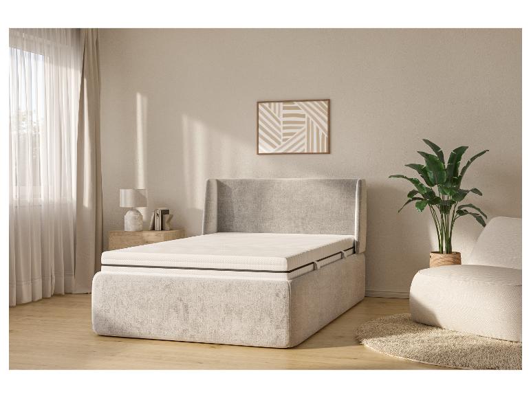 Lichte slaapkamer met beige gestoffeerd bed, nachtkastje, lamp en plant.