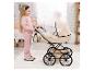 Meisje in roze duwt een beige poppenwagen met bijpassende tas in een kinderkamer.