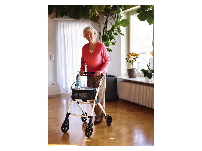 Een glimlachende oudere vrouw gebruikt een rollator met een fles water.