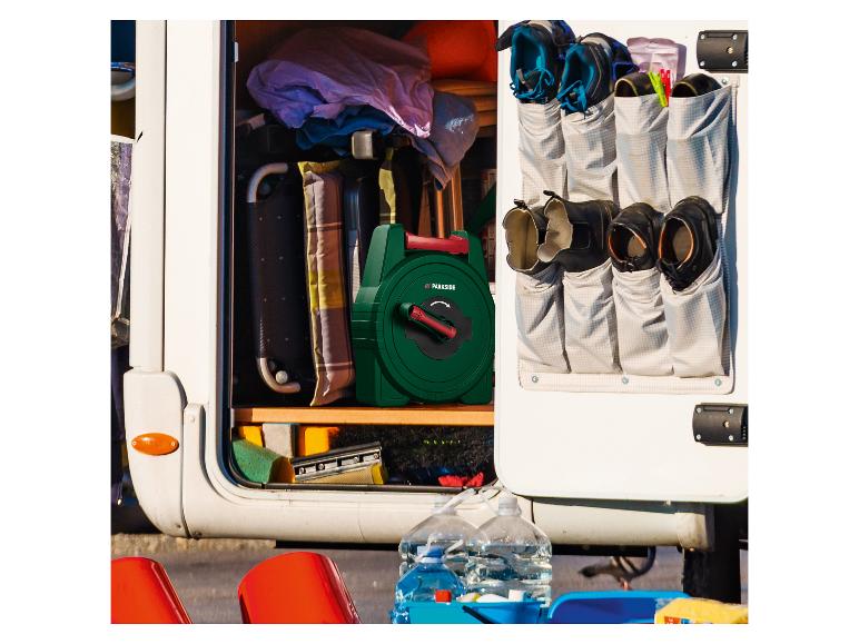 Open camperopslag met een groene slanghaspel, schoenen in een hangende organizer en schoonmaakspullen.