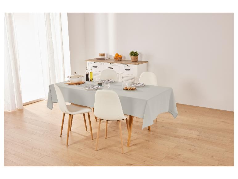 Grijze tafelkleed, stoelen en servies op een eettafel.