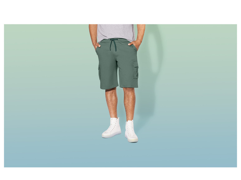 Man draagt ​​groene cargo-shorts en witte sneakers.