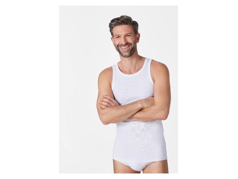 Een man draagt een wit tanktop en ondergoed.