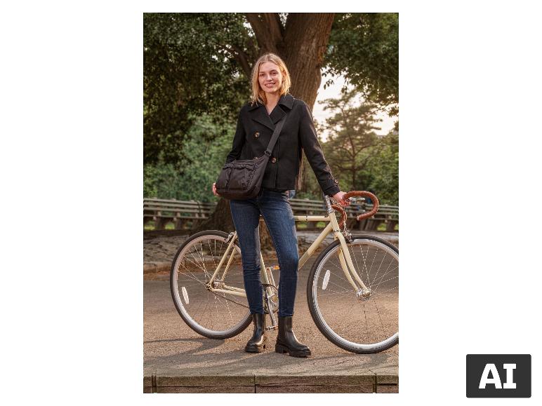 Vrouw in zwarte jas en jeans, met een fiets in een park.