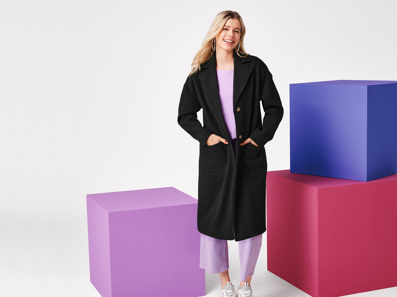 Een vrouw poseert in een zwarte jas, paarse broek en witte sneakers.