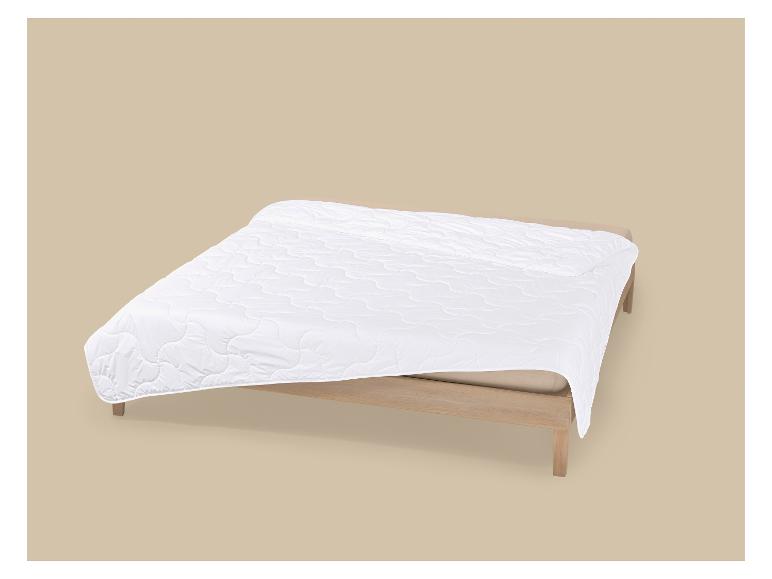 Wit gewatteerd dekbed op een houten bed met een beige achtergrond.