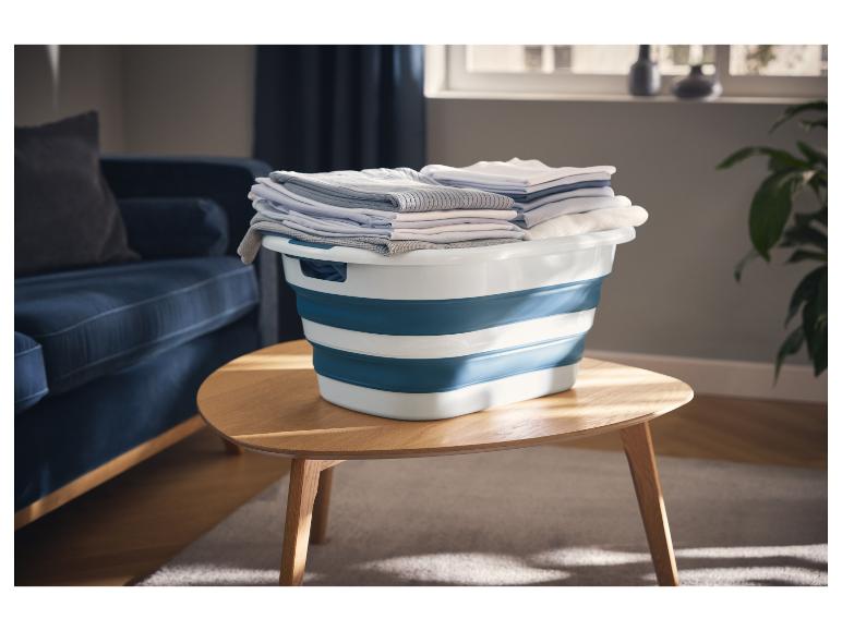 W5 opvouwbare wasmand met gevouwen kleding op een houten tafel in een woonkamer.
