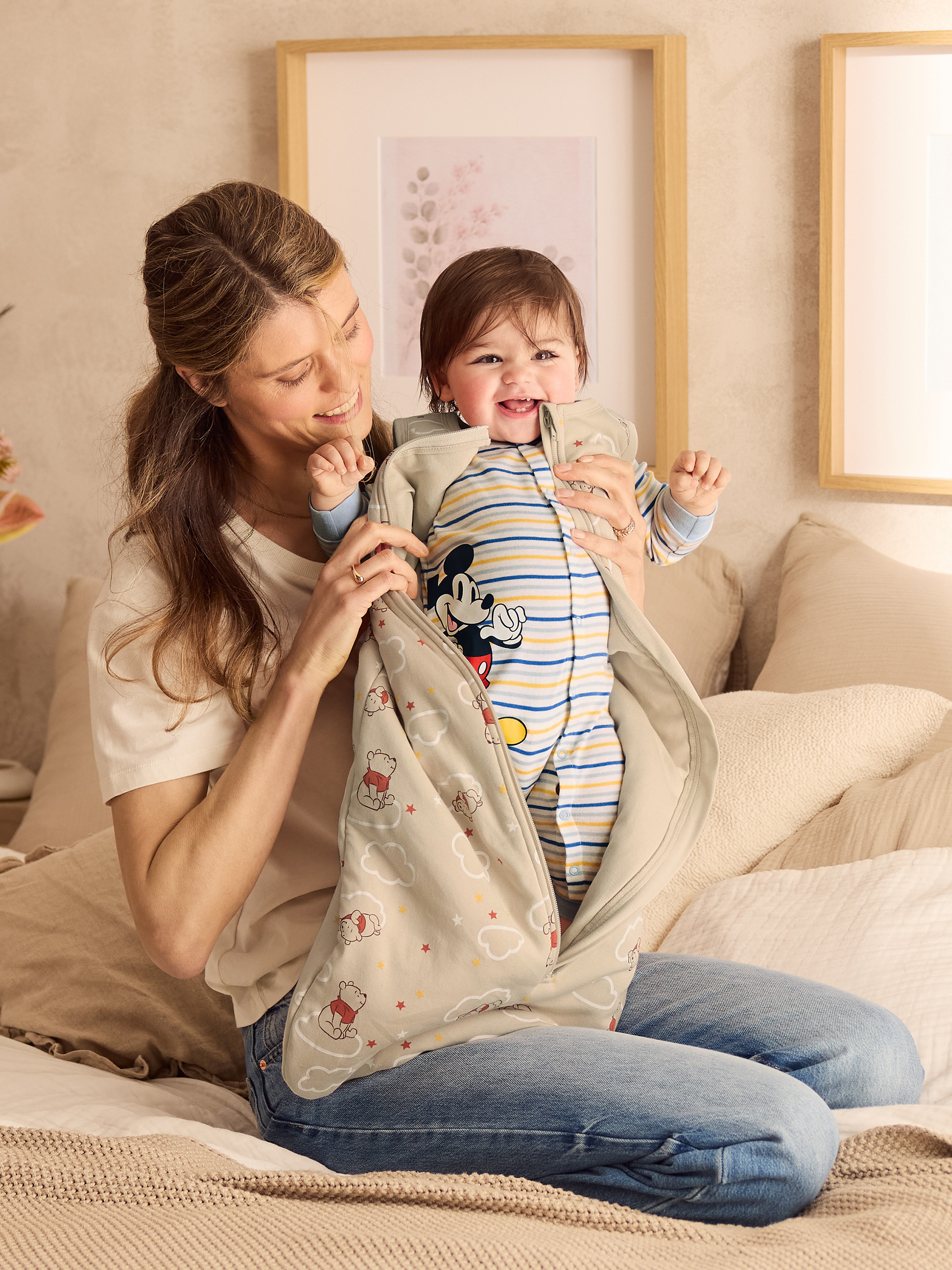 Lachende moeder houdt lachende baby vast in Winnie de Poeh-slaapzak.