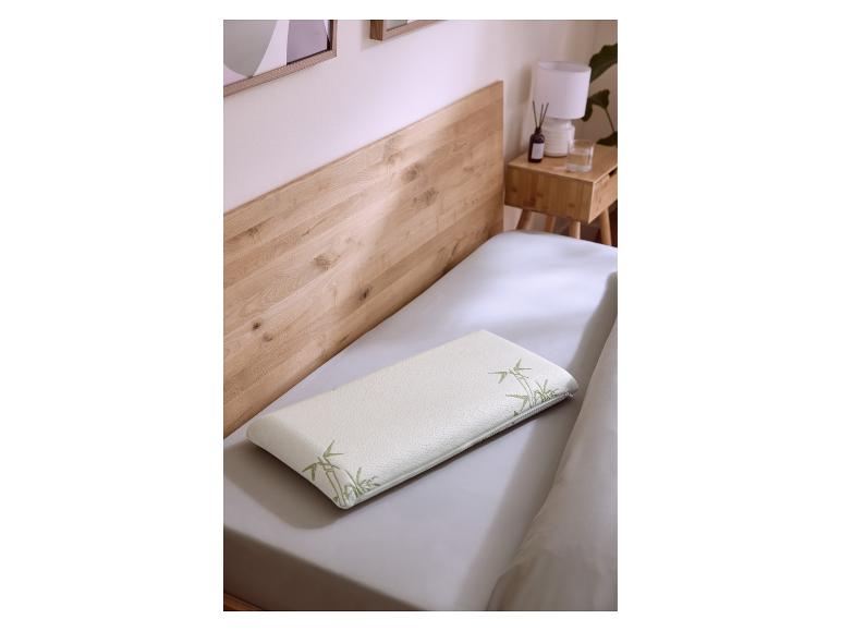 Wit kussen met bamboepatroon op een bed met houten hoofdbord en nachtkastje.