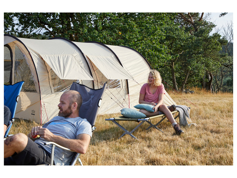 Twee personen relaxen buiten, één in een stoel en de ander op een campingbed, naast een Grand Canyon-tent.