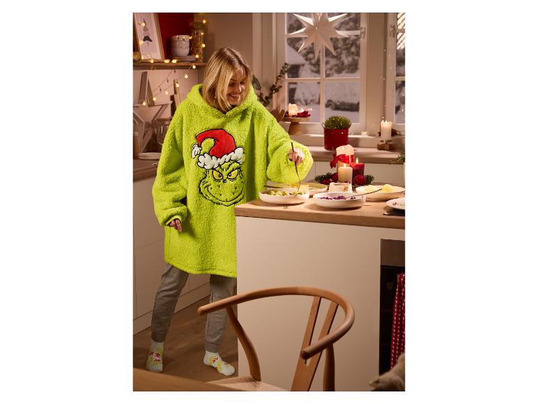 Vrouw in een oversized Grinch-hoodie bereidt eten in een kerstversierde keuken.