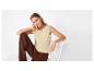 Vrouw in een beige top met borduursel en bruine broek, zittend op een witte stoel.