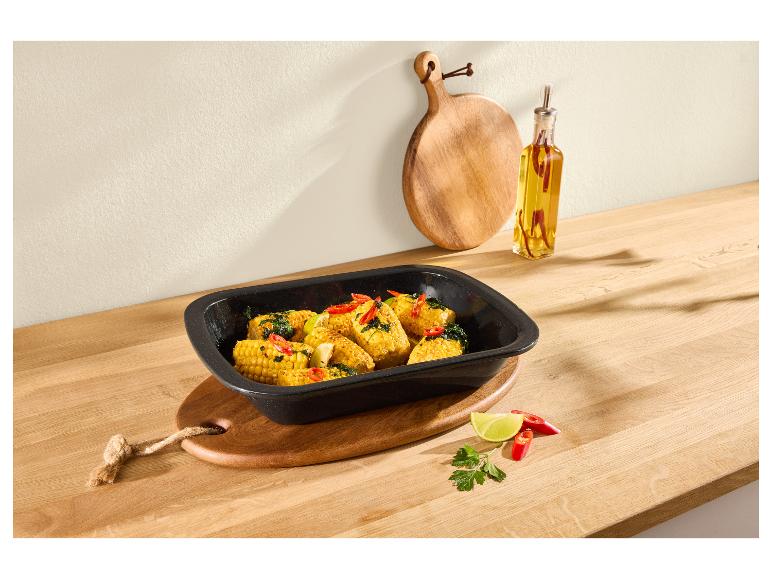 Geroosterde maïskolven met chili en limoen in een zwarte ovenschaal op een houten aanrecht.