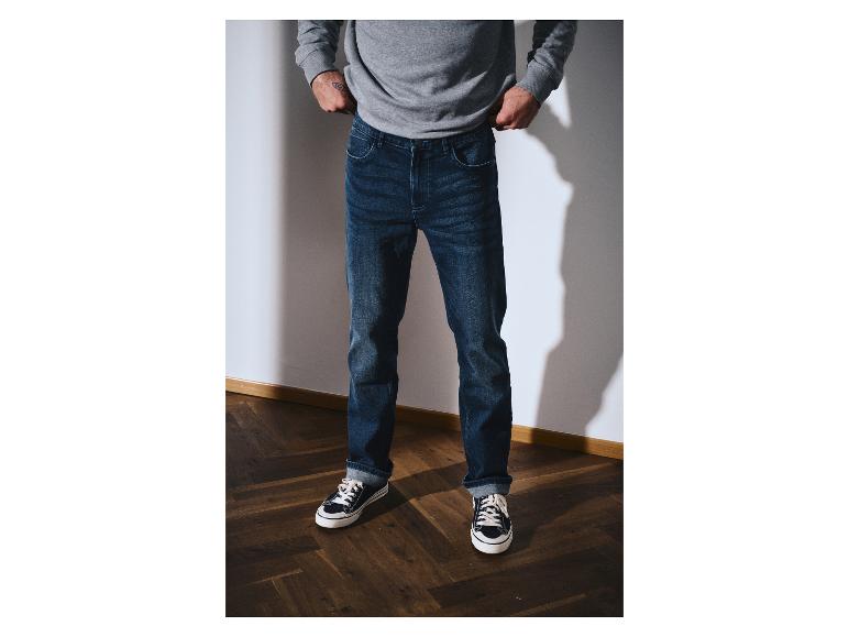 Man in een grijze sweater en donkerblauwe jeans met sneakers.