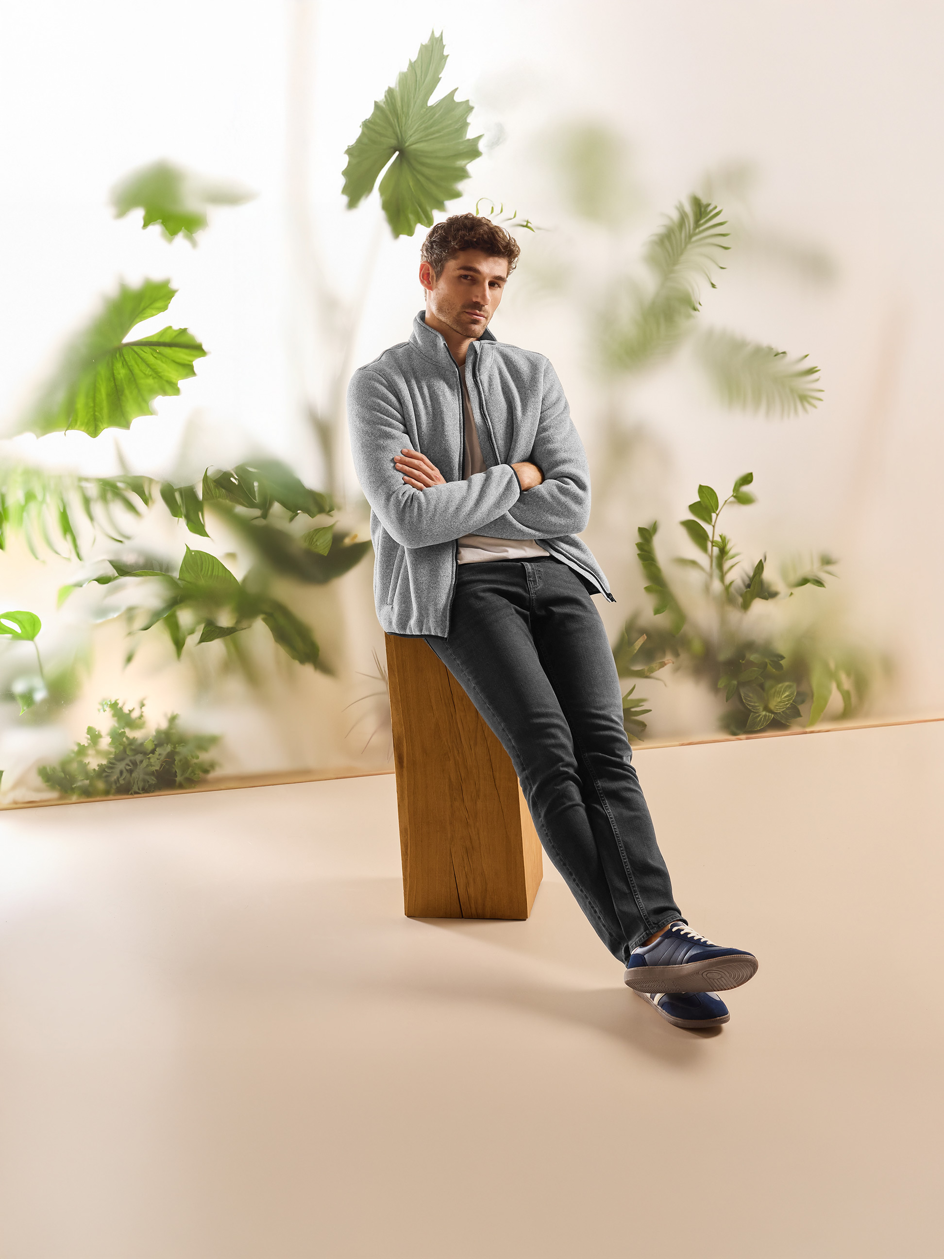 Man in grijs fleecevest en donkere jeans, zittend in een natuurlijke omgeving.