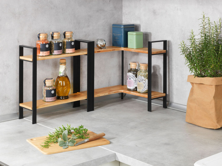 Een houten hoekrek met zwarte metalen poten, gevuld met kruiden, specerijen en een fles olie.