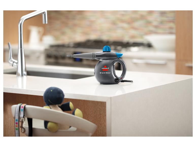Bissell Steam Shot stoomreiniger op een aanrecht met een kraan en speelgoed op de achtergrond.