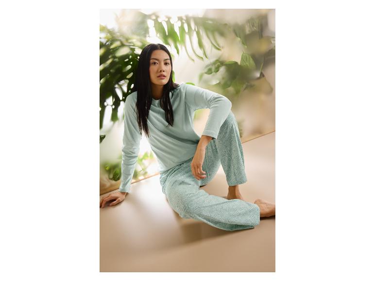 Vrouw in lichtblauwe pyjama met bladpatroon, zittend op de grond voor planten.