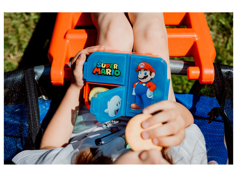 Een kind eet een snack uit een Super Mario lunchbox.