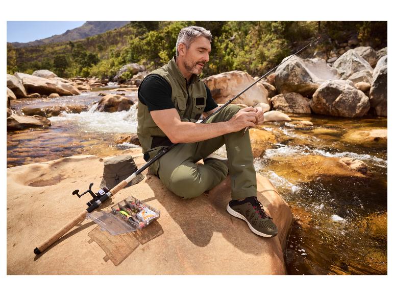 Man vist in een rivier, draagt visvest en -broek, bereidt aas voor.