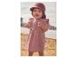 Baby in een roze jurk en zonnehoed, staand op een zandstrand.