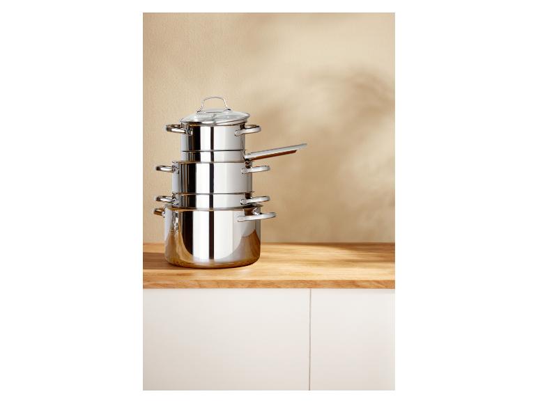 Een stapel roestvrijstalen potten en pannen met deksels op een houten aanrecht.