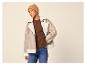 Vrouw in beige pilotenjack, bruine trui, blauwe jeans en mosterdkleurige muts.