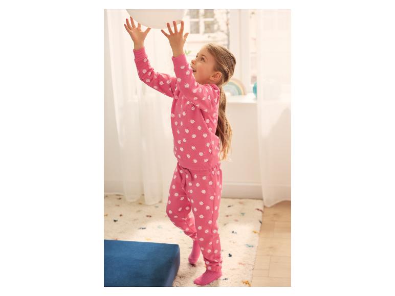 Meisje in roze pyjama met madeliefjesprint speelt binnen met een witte ballon.