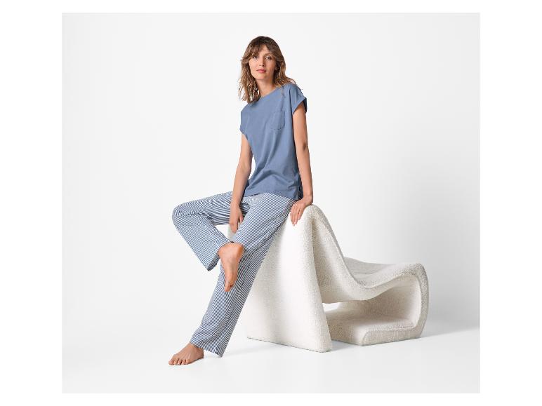 Vrouw in blauw T-shirt en gestreepte broek zit op een witte stoel.