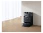 Zwarte robotstofzuiger met laadstation in een kamer met witte gordijnen en houten vloer.