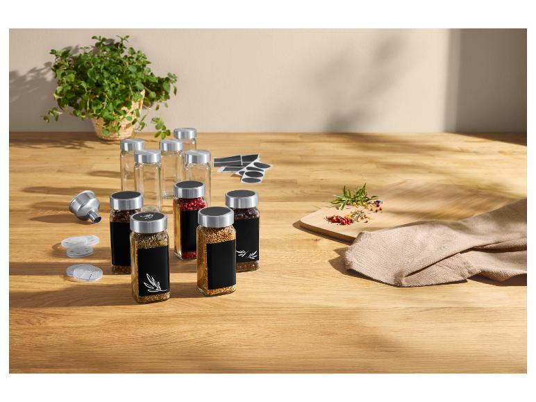 Kruiden in glazen potten met zwarte etiketten, trechter en verse kruiden op houten tafel.