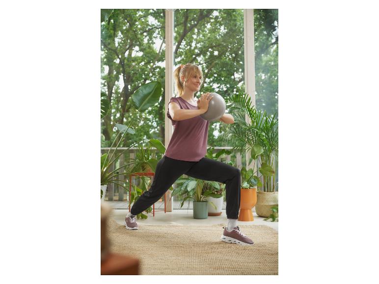 Vrouw in sportkleding doet lunge met grijze bal op terras.
